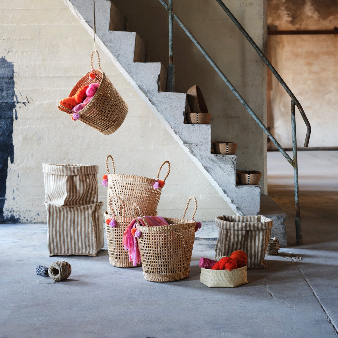 Baskets from the MÄVINN collection made of natural materials have been arranged in and around a concrete floor and staircase.