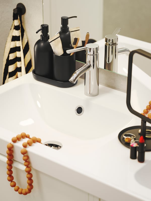 An orange bead necklace is hanging over the edge of a white ORRSJÖN wash-basin and there are makeup products on the side.