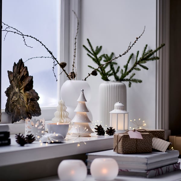 A windowsill is decorated for the holidays with white-themed VINTERFINT ornaments and a STRÅLA lighting chain.